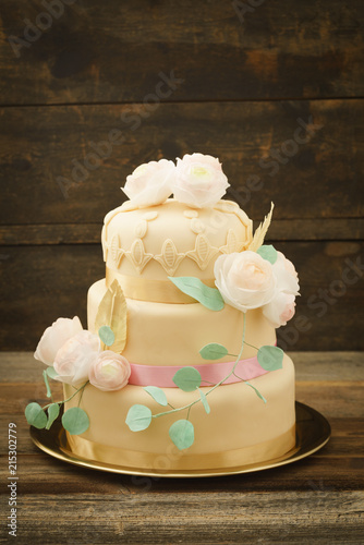 Three tiered wedding cake with fondant and ranunculus flowers, leaves and feathers made of wafer paper