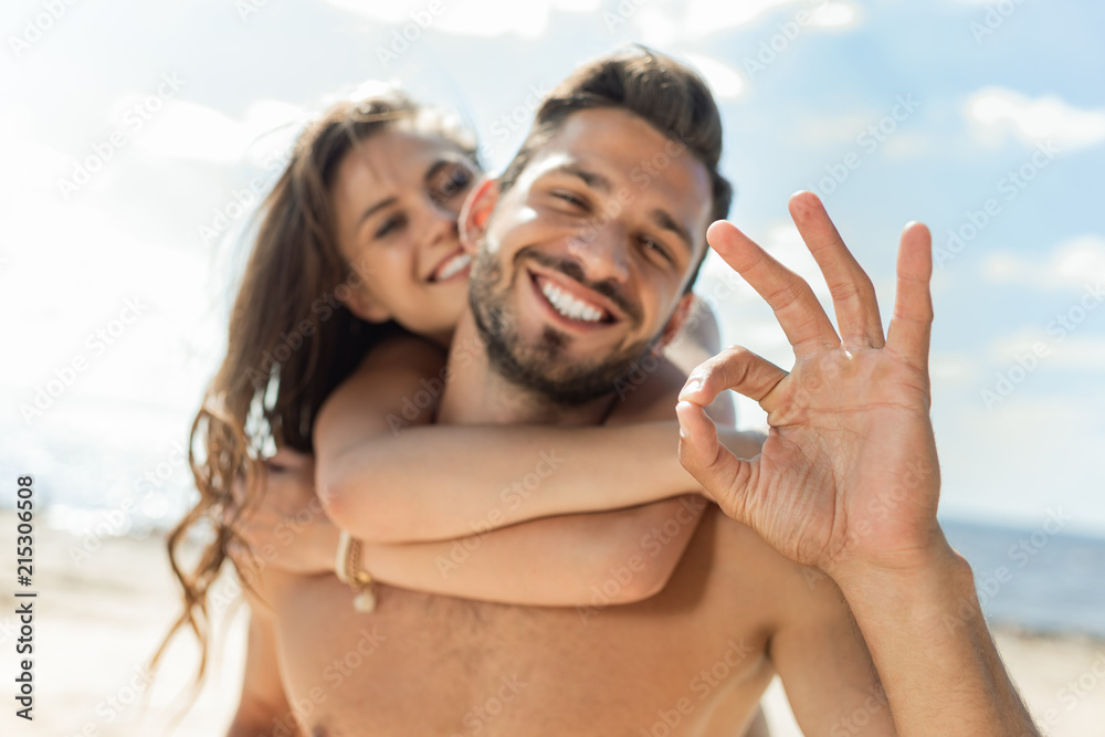 selective focus of man showing ok sign and piggybacking his girlfriend selective focus of man showing ok sign and piggybacking his girlfriend