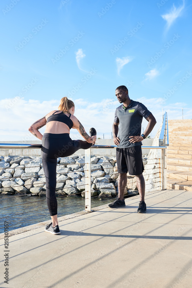 Sportswoman stretching with personal trainer on riverbank. Sportswoman stretching with personal trainer on riverbank.