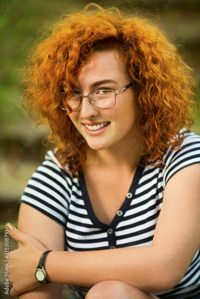 Fototapeta premium Young woman with ginger hair sitting on a steps in a park