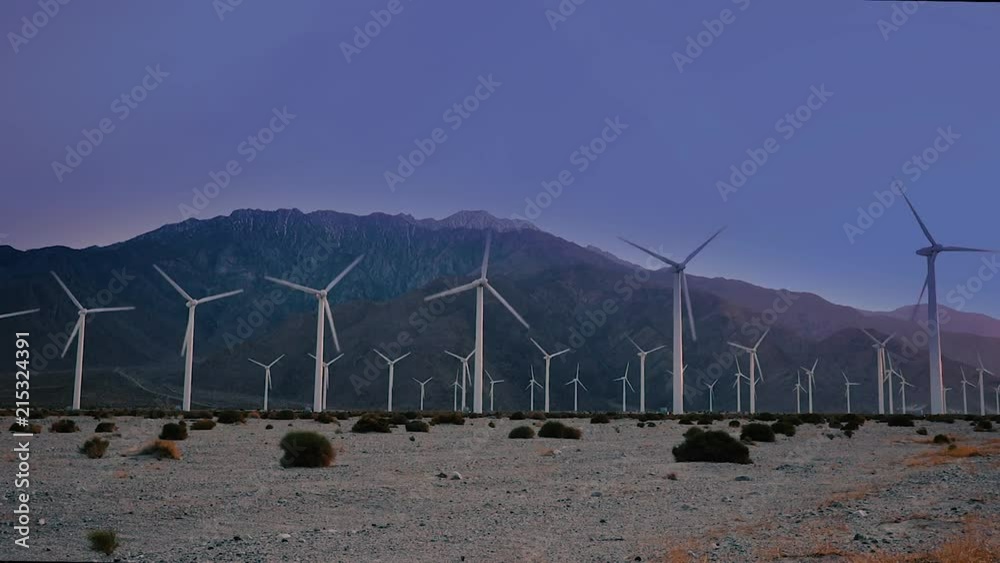 Windmills spinning at sunset in a dry desert with mountain range in background. TILT start into static composition.