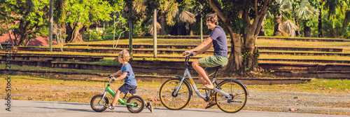 Happy family is riding bikes outdoors and smiling. Father on a bike and son on a balancebike BANNER, long format photo