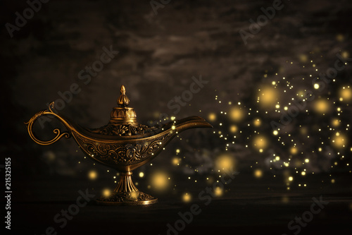 Image of magical mysterious aladdin lamp with glitter sparkle lights over black background. Lamp of wishes.