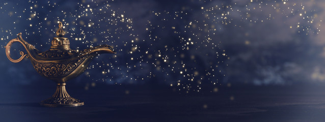 Image of magical mysterious aladdin lamp with glowing glitter lights over black background. Lamp of wishes.