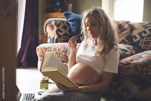 Pregnant woman reading a book in living room photo
