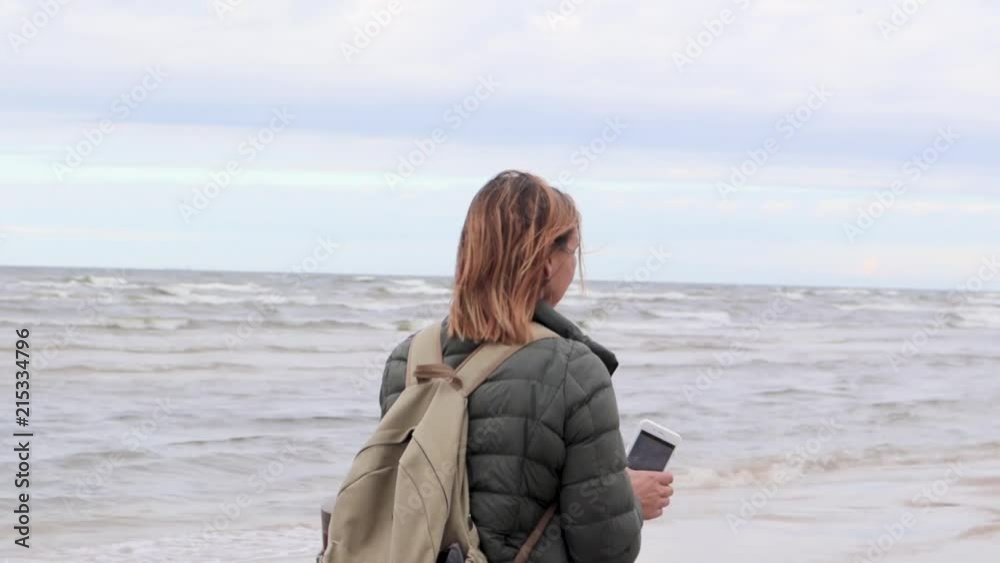 Young woman walking a beach with the phone in hands and taking picture of the sea. Young woman walking a beach with the phone in hands and taking picture of the sea.