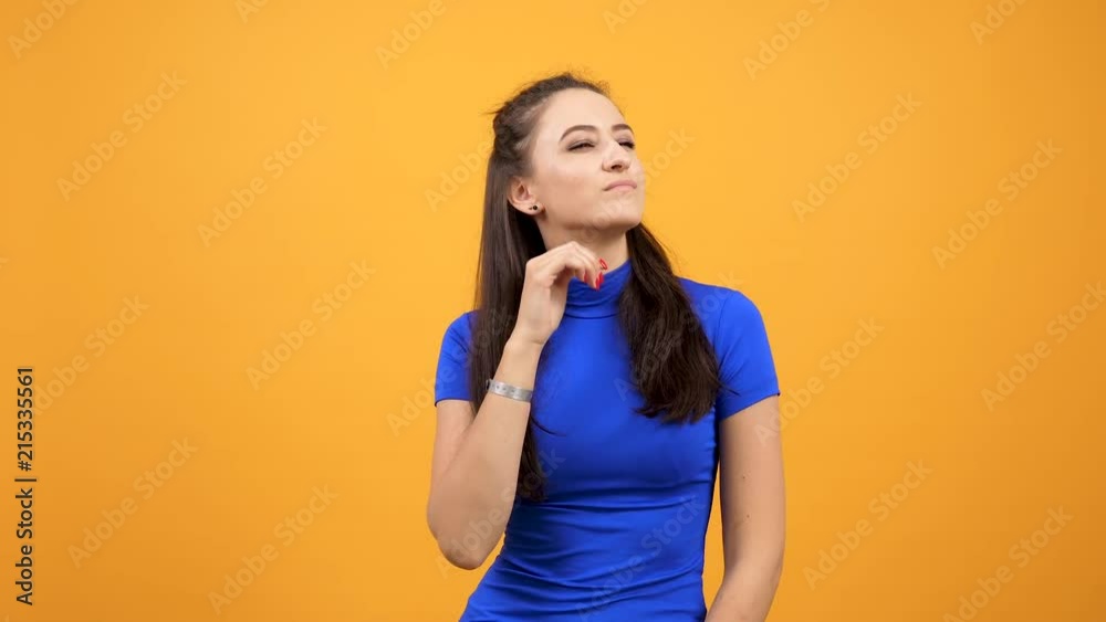 Beautiful woman in blue t-shirt being bored on vivid orange background in studio. Arrogant girl Beautiful woman in blue t-shirt being bored on vivid orange background in studio. Arrogant girl