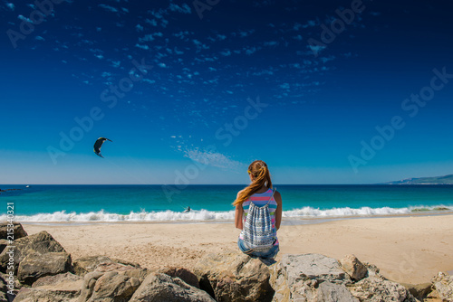  girl is sitting on the ocean. Woman sits back and looks at the sea. Kite surfing. Active rest on the beach. Kitesurfing. paragliding on the waves
