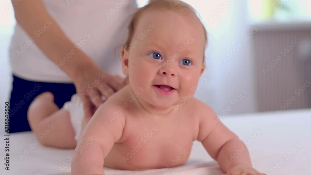 Adorable newborn baby with beautiful blue eyes lies on belly while mother giving a massage Adorable newborn baby with beautiful blue eyes lies on belly while mother giving a massage