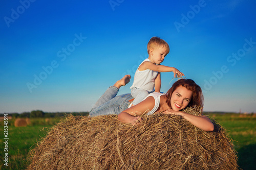 Mom lies on a haystack in the field, and the son sits at the mother's back