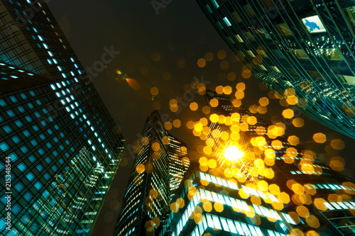 Illuminated office buildings in Paris business district La Defense. Night city lights, skyscrapers glass facades. Modern urban architecture, economy, finances, business activity concept. Lens flare