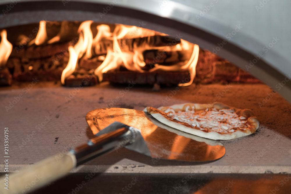 The working furnace for preparation of pizza. Inside burns firewood and big fire rises, on a shovel in the furnace put cheese pizza. Reflections of a flame on a surface