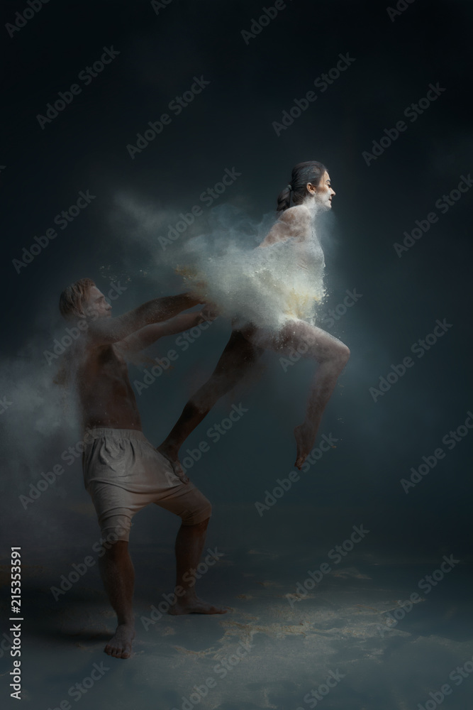 Dancing in flour concept. Girl woman female and muscle fitness guy man male couple in love and in relationship making dance element prefomance in flour / white dust on isolated black / grey background