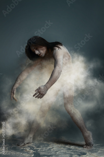 Dancing in flour concept. Muscle fitness guy man male dancer in dust / fog. Guy wearing white shorts making dance element perfomance in flour cloud on isolated grey / black background