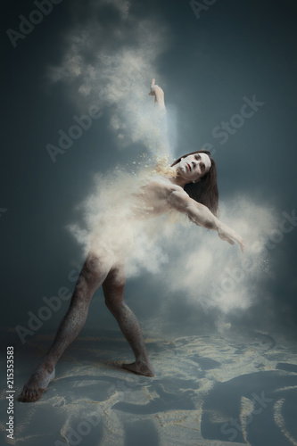 Dancing in flour concept. Muscle fitness guy man male dancer in dust / fog. Guy wearing white shorts making dance element in flour cloud on isolated grey / black background