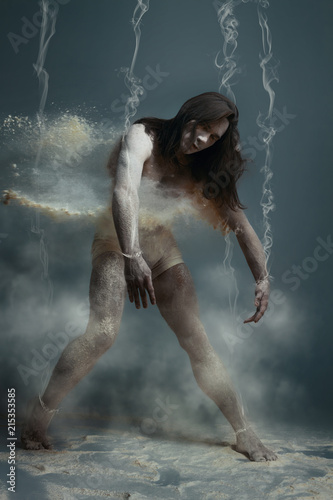 Dancing in flour concept. Muscle fitness guy man male dancer in dust / fog. Guy wearing white shorts making dance element in flour cloud on isolated grey / black background. Dependence concept
