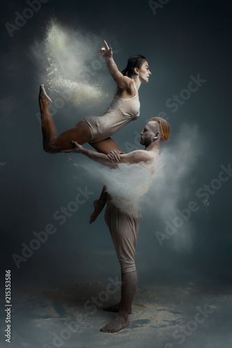 Dancing in flour concept. Girl woman female and muscle fitness guy man male couple in love and in relationship making dance element prefomance in flour / white dust on isolated black / grey background