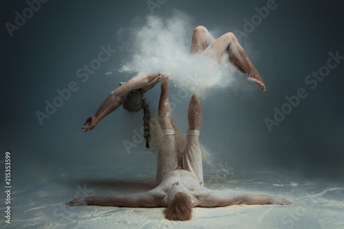 Dancing in flour concept. Girl woman female and muscle fitness guy man male couple in love and in relationship making dance element prefomance in flour / white dust on isolated black / grey background