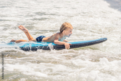 Happy baby boy - young surfer ride on surfboard with fun on sea waves. Active family lifestyle, kids outdoor water sport lessons and swimming activity in surf camp. Summer vacation with child photo