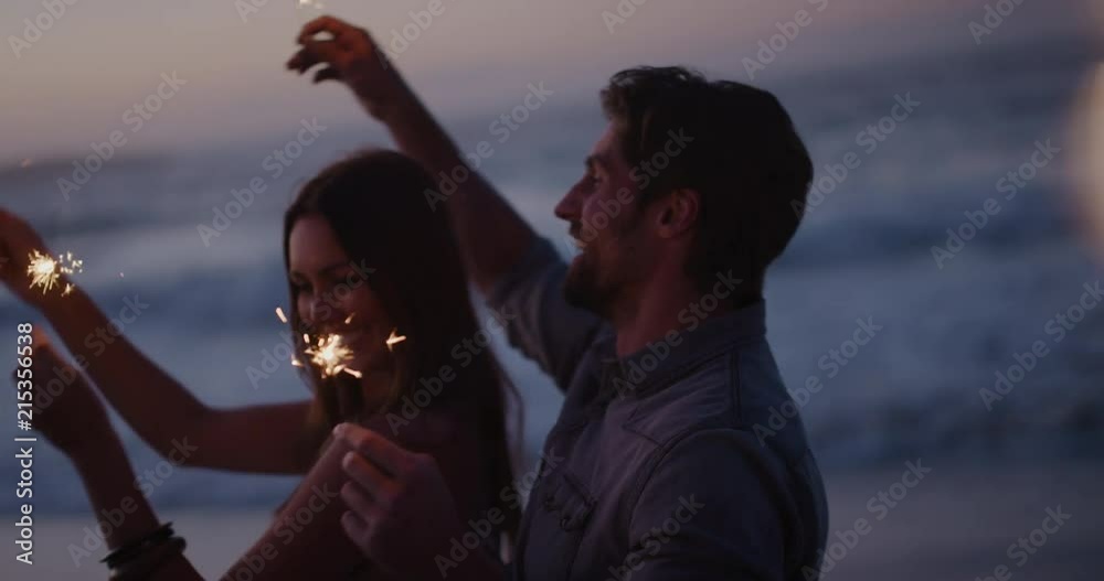 happy young couple waving sparklers dancing celebrating new years eve on calm beach sunset background sparkle firework
