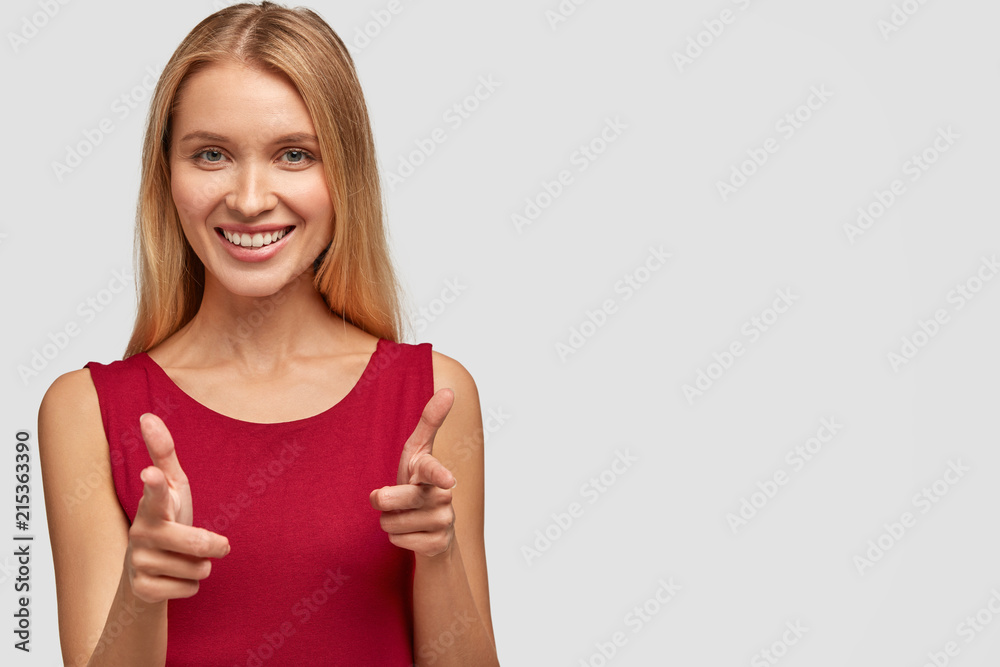 Pretty cute young female with happy expression, points at you or makes gun shoot with fingers, wears red casual vest, isolated over white background with copy space for your advertising content Pretty cute young female with happy expression, points at you or makes gun shoot with fingers, wears red casual vest, isolated over white background with copy space for your advertising content