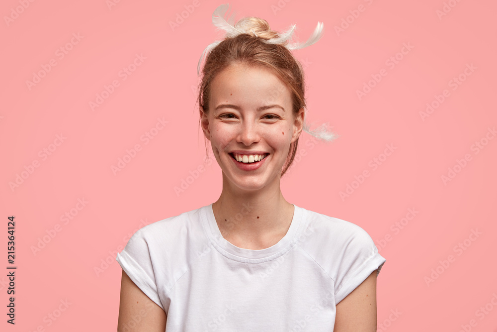 Studio shot of happy female wakes up early at morning in good mood, has appealing look, wears casual t shirt, isolated over pink wall. Glad woman rejoices weekend enjoys long sleep and pleasant dreams