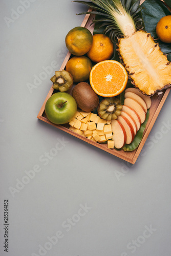 Assorted fresh fruits on plate. Apple, orange, kiwi, pineapple, tangerines on wooden plate. Top view