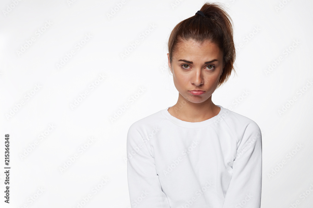 Waist up portrait of miserable gloomy brunette female looks offended, frowns face in displeasure, hears unpleasant comments. Young woman in casual sweatshirt pouting lips being abused by friends. Waist up portrait of miserable gloomy brunette female looks offended, frowns face in displeasure, hears unpleasant comments. Young woman in casual sweatshirt pouting lips being abused by friends.