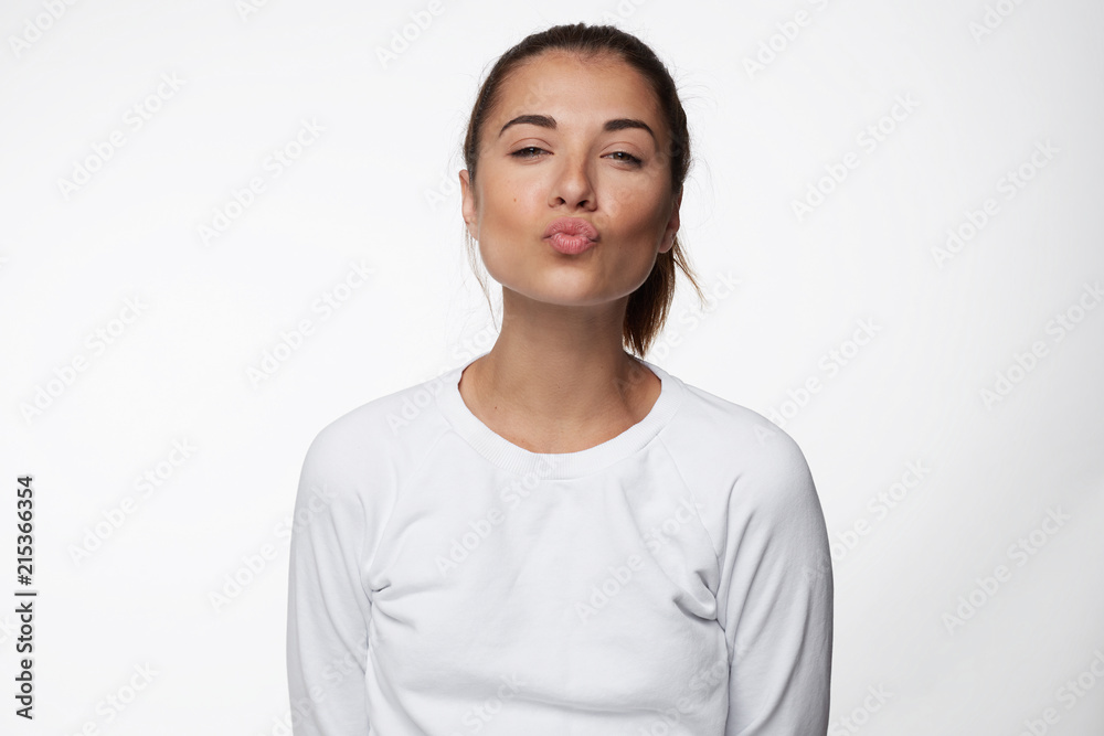 First kisses always tempting. Portrait of joyful satisfied good-looking woman, pulling face with folded lips, closed eyes towards camera, wanting to kiss or give mwah boyfriend over white blank wall. First kisses always tempting. Portrait of joyful satisfied good-looking woman, pulling face with folded lips, closed eyes towards camera, wanting to kiss or give mwah boyfriend over white blank wall.