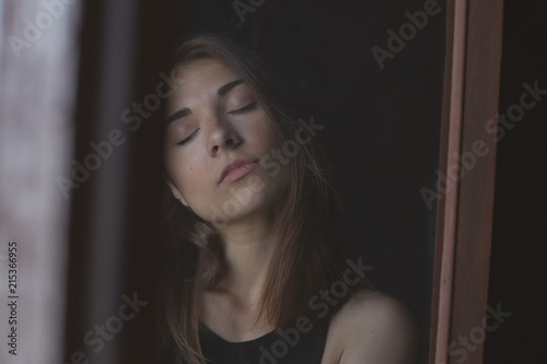 Sensual authentic portrait of young serious lady posing through dirty window, communicating with camera. Real life and art concept. Human feelings, emotions and expressions in natural conditions.
