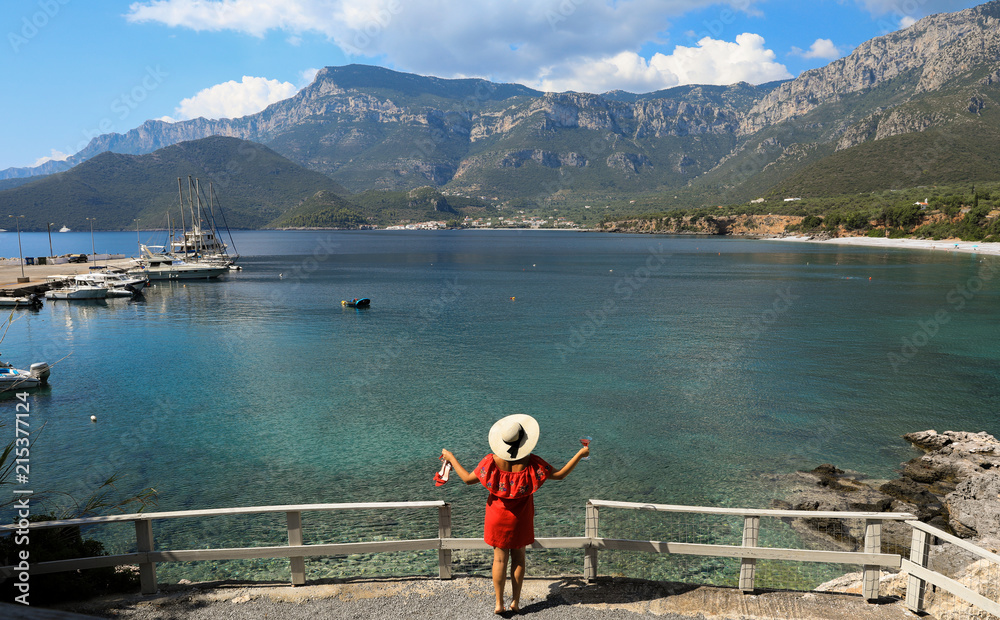 Summer holidays relaxing woman in a red dress with glass of red martini on the background of a picturesque seascape, vacation concept.