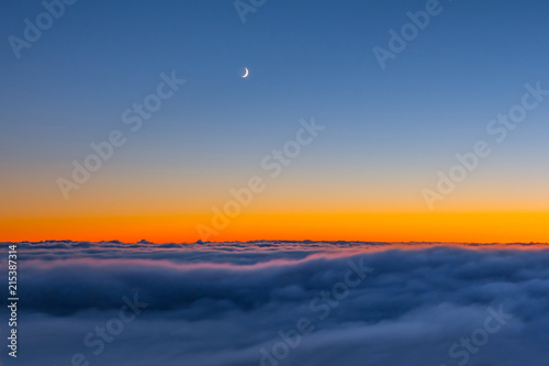 Fototapeta dense clouds above mountain ridge at the dusk with half moon on a sky