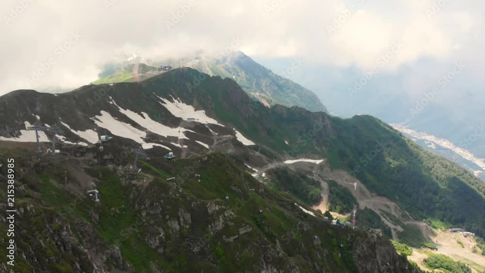 Flight of the camera over mountains. Aibga Ridge. Cable car with cabins on snow background. Mountains near the ski resort of Rosa Khutor in Krasnaya Polyana. Sochi. Flight of the camera over mountains. Aibga Ridge. Cable car with cabins on snow background. Mountains near the ski resort of Rosa Khutor in Krasnaya Polyana. Sochi.