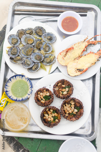 Vietnamese local seafood with grilled lobster, snail, fish salad and echinus on beach.