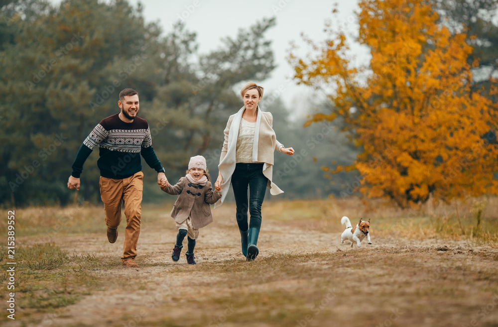 Parents with their daughter hold hands and run at forest path with dog in autumn forest. Parents with their daughter hold hands and run at forest path with dog in autumn forest.