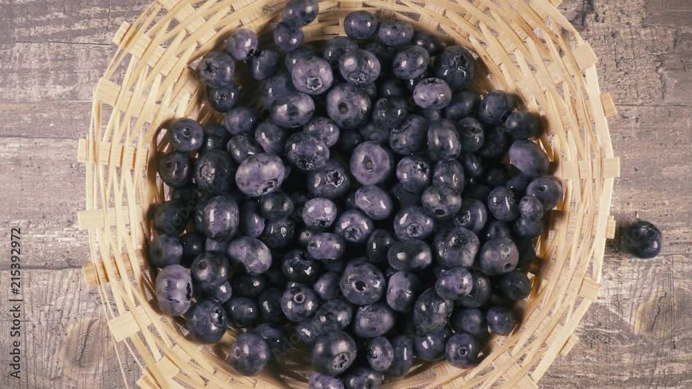 Slow motion blueberries fall into a wicker basket on a wooden table top view Slow motion blueberries fall into a wicker basket on a wooden table top view