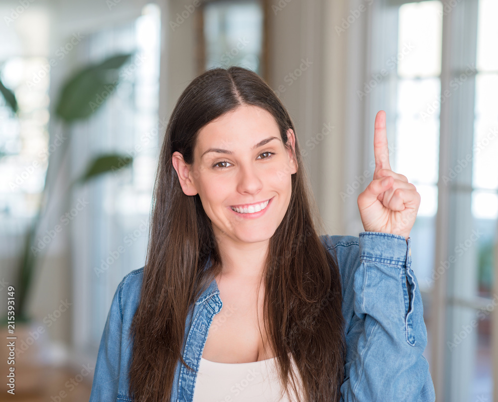 Young beautiful woman at home surprised with an idea or question pointing finger with happy face, number one
