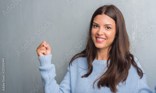 Young brunette woman over grunge grey wall screaming proud and celebrating victory and success very excited, cheering emotion photo