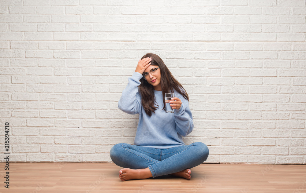 Young brunette woman sitting on the floor drinking glass of water stressed with hand on head, shocked with shame and surprise face, angry and frustrated. Fear and upset for mistake. Young brunette woman sitting on the floor drinking glass of water stressed with hand on head, shocked with shame and surprise face, angry and frustrated. Fear and upset for mistake.