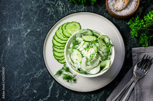 Creamy cucumber dill salad with yogurt dressing on dark marble background. Top view  space for text.
