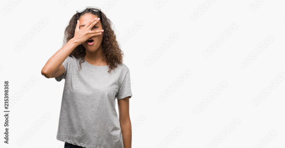 Beautiful young hispanic woman wearing glasses peeking in shock covering face and eyes with hand, looking through fingers with embarrassed expression. Beautiful young hispanic woman wearing glasses peeking in shock covering face and eyes with hand, looking through fingers with embarrassed expression.