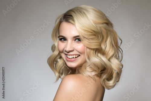 Blonde with curls on a gray background, natural make-up and clean skin. beautiful smile and big eyes. Portrait