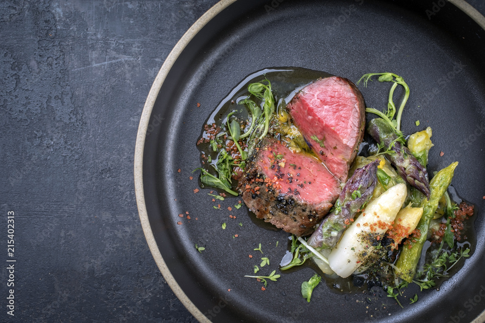 Modern German asparagus potato salad with barbecue dry aged sliced fillet steak and herbs as closeup on a plate with copy space left Modern German asparagus potato salad with barbecue dry aged sliced fillet steak and herbs as closeup on a plate with copy space left