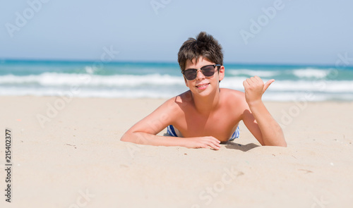 Young child on holidays at the beach pointing and showing with thumb up to the side with happy face smiling
