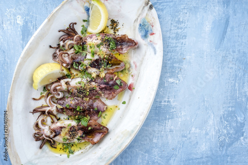 Traditionell gegrillte griechische Calamari mit Käutern und Zitrone als Draufsicht auf einem Teller mit Textfreiraum rechts photo