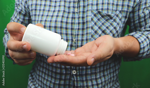 Mans hands with pills on, spilling pills out of bottle on green background