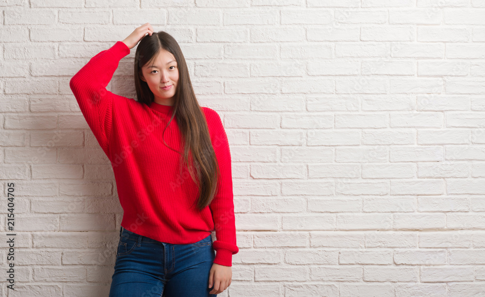 Young Chinese woman over brick wall confuse and wonder about question. Uncertain with doubt, thinking with hand on head. Pensive concept. Young Chinese woman over brick wall confuse and wonder about question. Uncertain with doubt, thinking with hand on head. Pensive concept.
