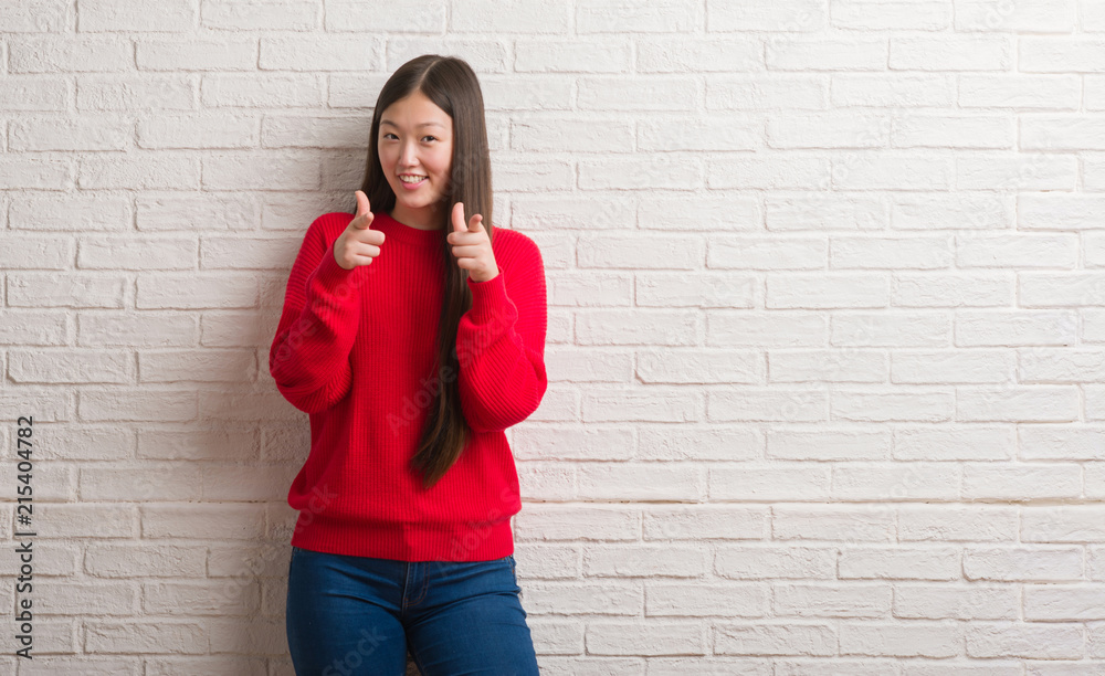 Young Chinese woman over brick wall pointing fingers to camera with happy and funny face. Good energy and vibes. Young Chinese woman over brick wall pointing fingers to camera with happy and funny face. Good energy and vibes.