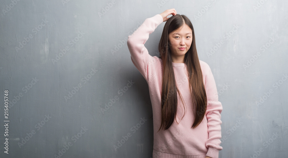 Young Chinese woman over grey wall confuse and wonder about question. Uncertain with doubt, thinking with hand on head. Pensive concept. Young Chinese woman over grey wall confuse and wonder about question. Uncertain with doubt, thinking with hand on head. Pensive concept.