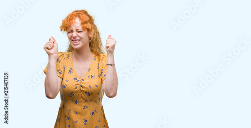 Young redhead woman excited for success with arms raised celebrating victory smiling. Winner concept.